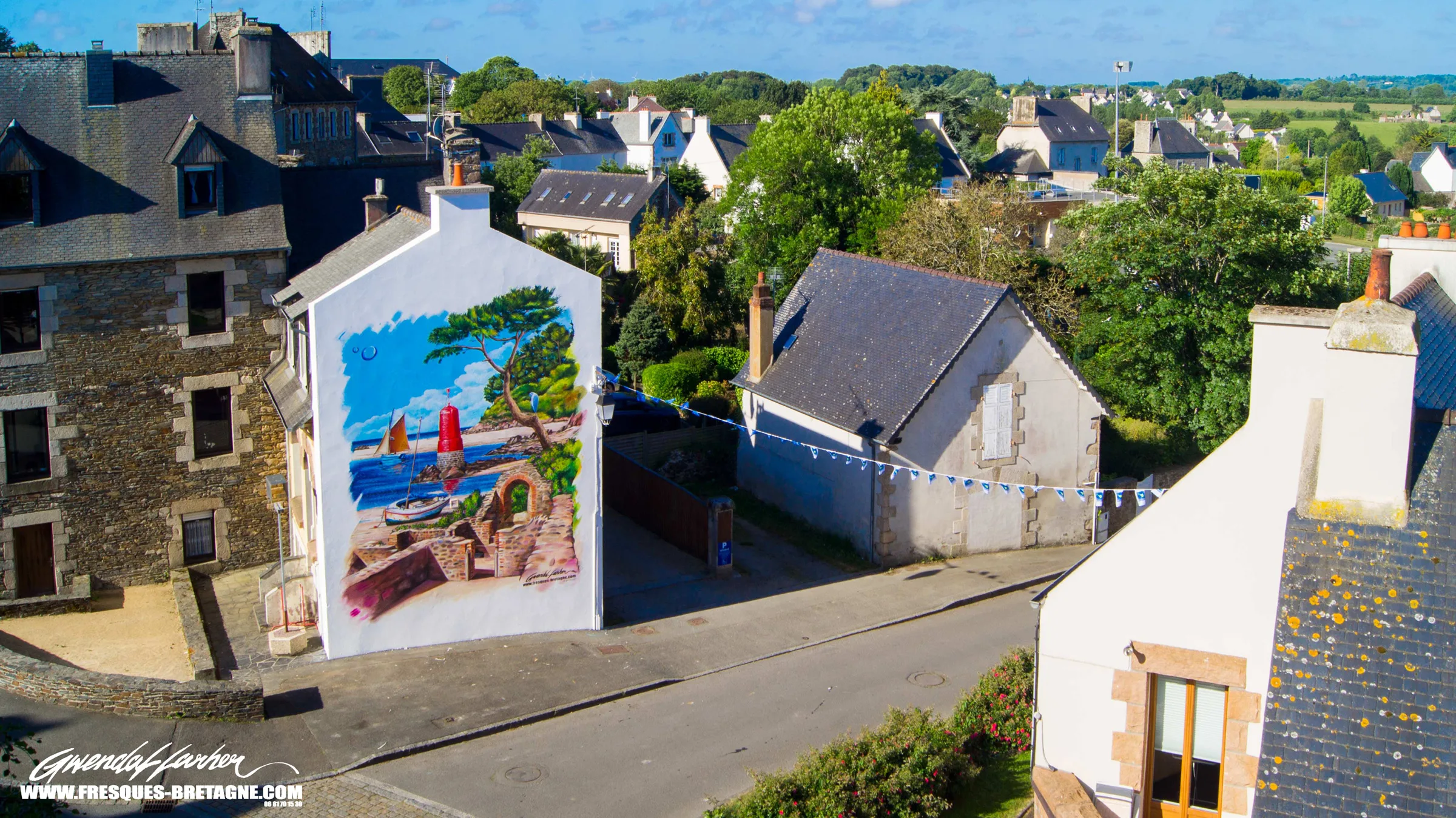 Fresque monumentale en trompe-l'œil sur un pignon d'immeuble en centre-ville, phare rouge, voilier et pin dans une crique, vue aérienne de la commune de Plestin-les-Grèves